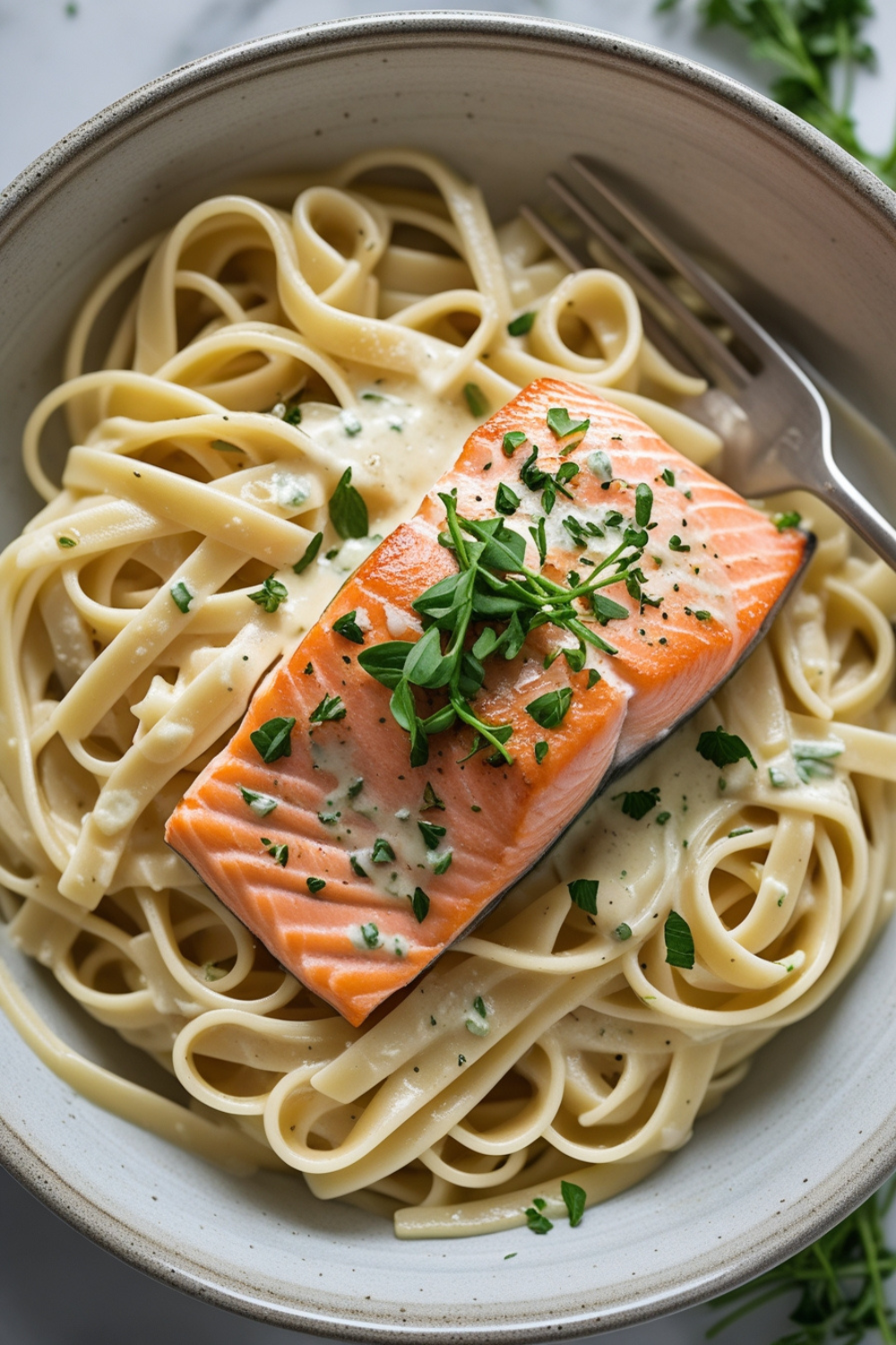 A bowl of silky fettuccine coated in a creamy garlic parmesan sauce, topped with flakey salmon and a sprinkle of fresh herbs. It looks like something straight out of a cozy bistro, but it took you just 15 minutes to make!