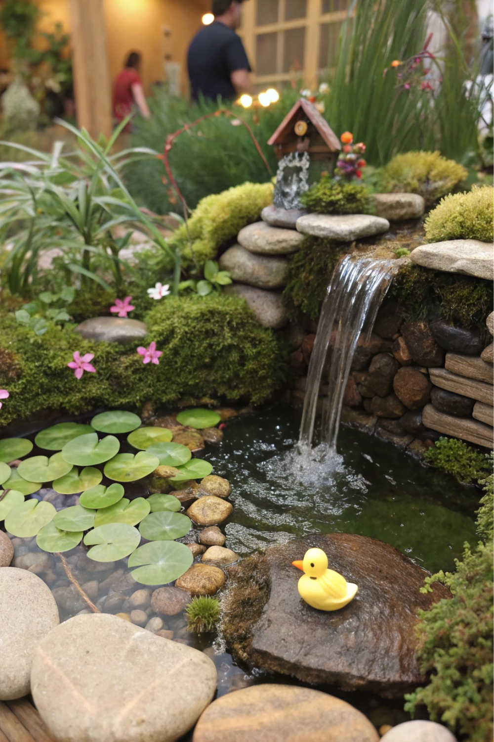 A tiny pond with floating lily pads and a tiny duck figurine. A fairy-size waterfall trickles over pebbles