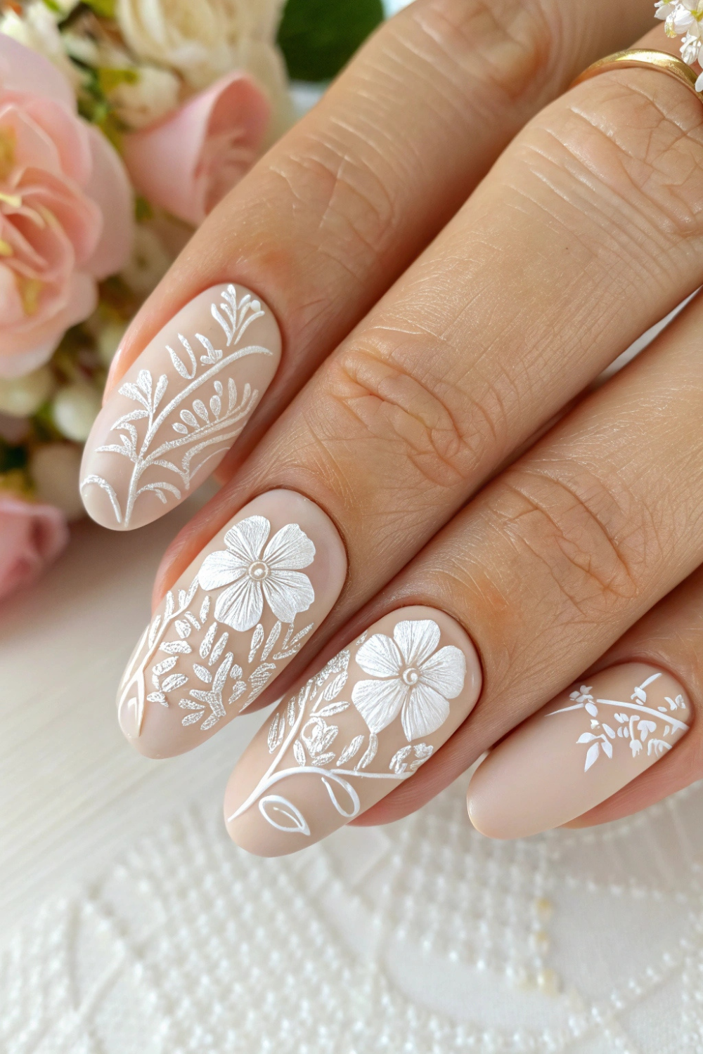 A soft nude base with 3D embossed floral details in white, giving a lace-like effect. These nails look like elegant spring wedding nails with their delicate, romantic finish.